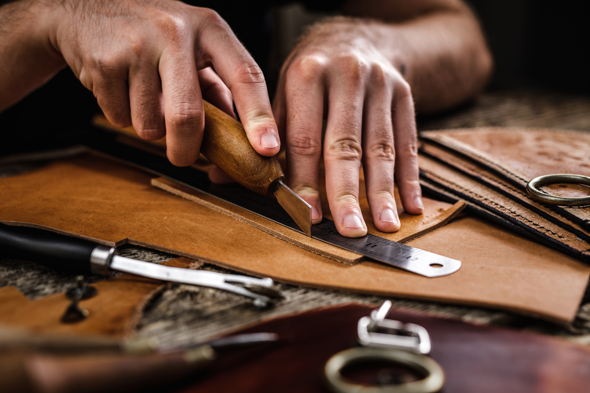 Leather craft tools on the old wood table in a shed. Leather craftsman workspace. Grounge dark wood texture background.